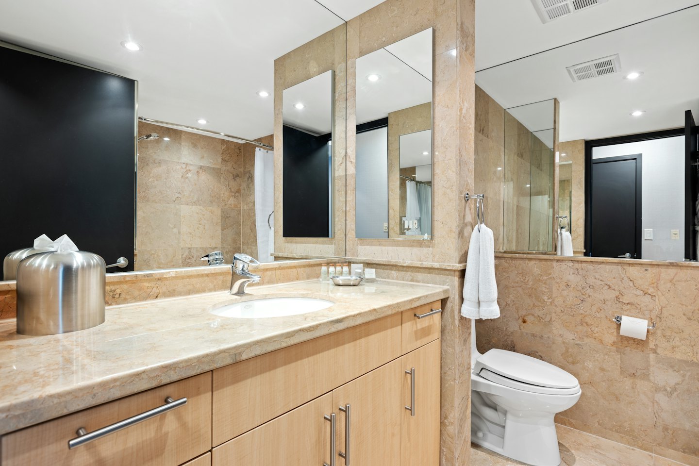 Bagno moderno con mobile in legno chiaro e piano in marmo.