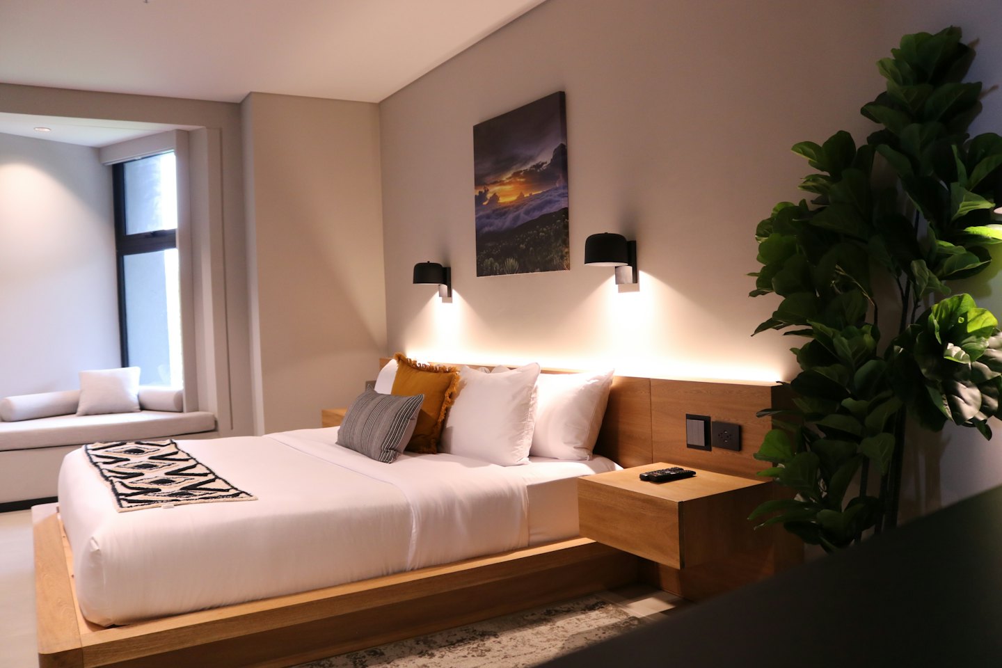 Camera d'albergo moderna con lenzuola bianche e una pianta verde.